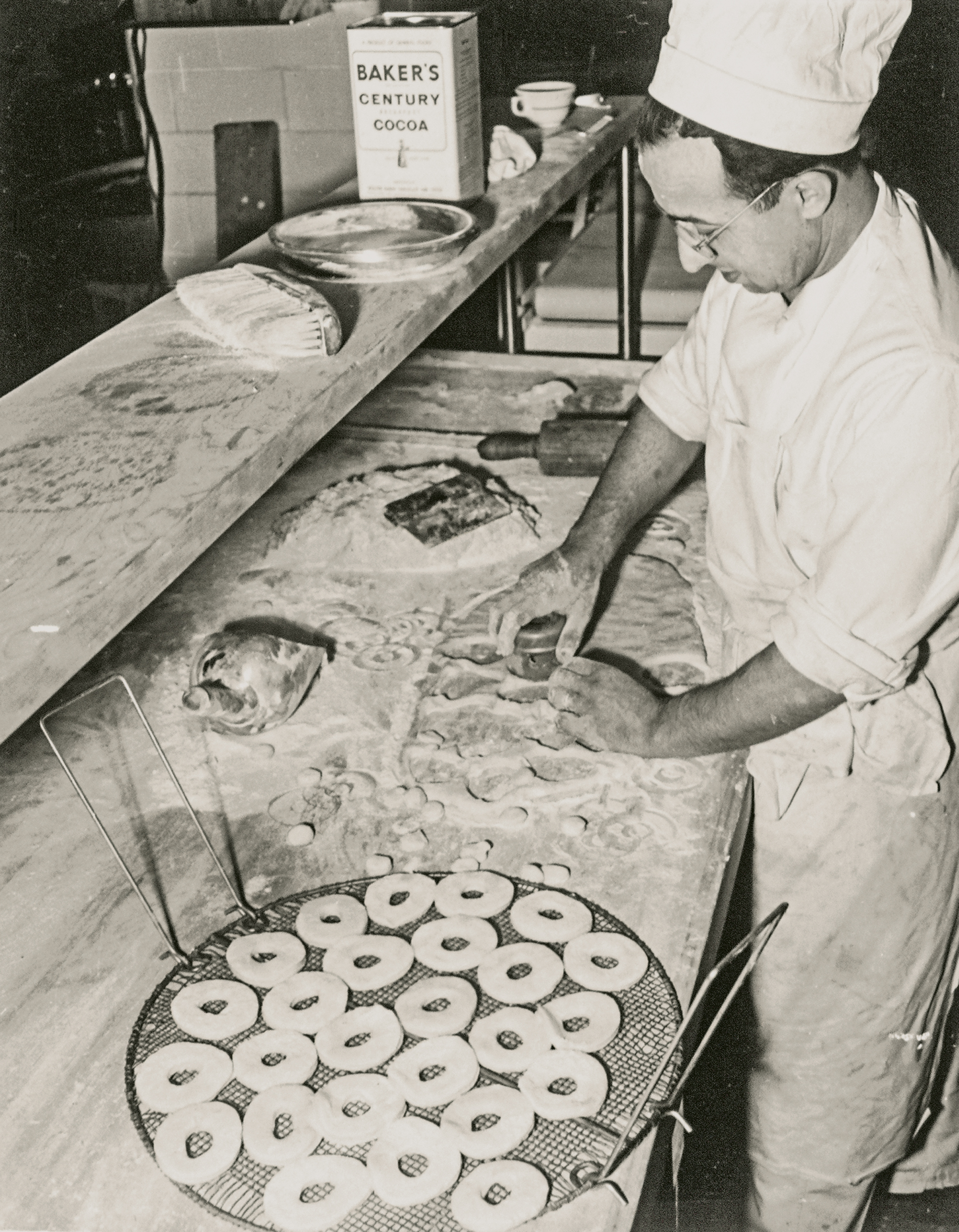 A baker cuts doughnuts in the 1950s